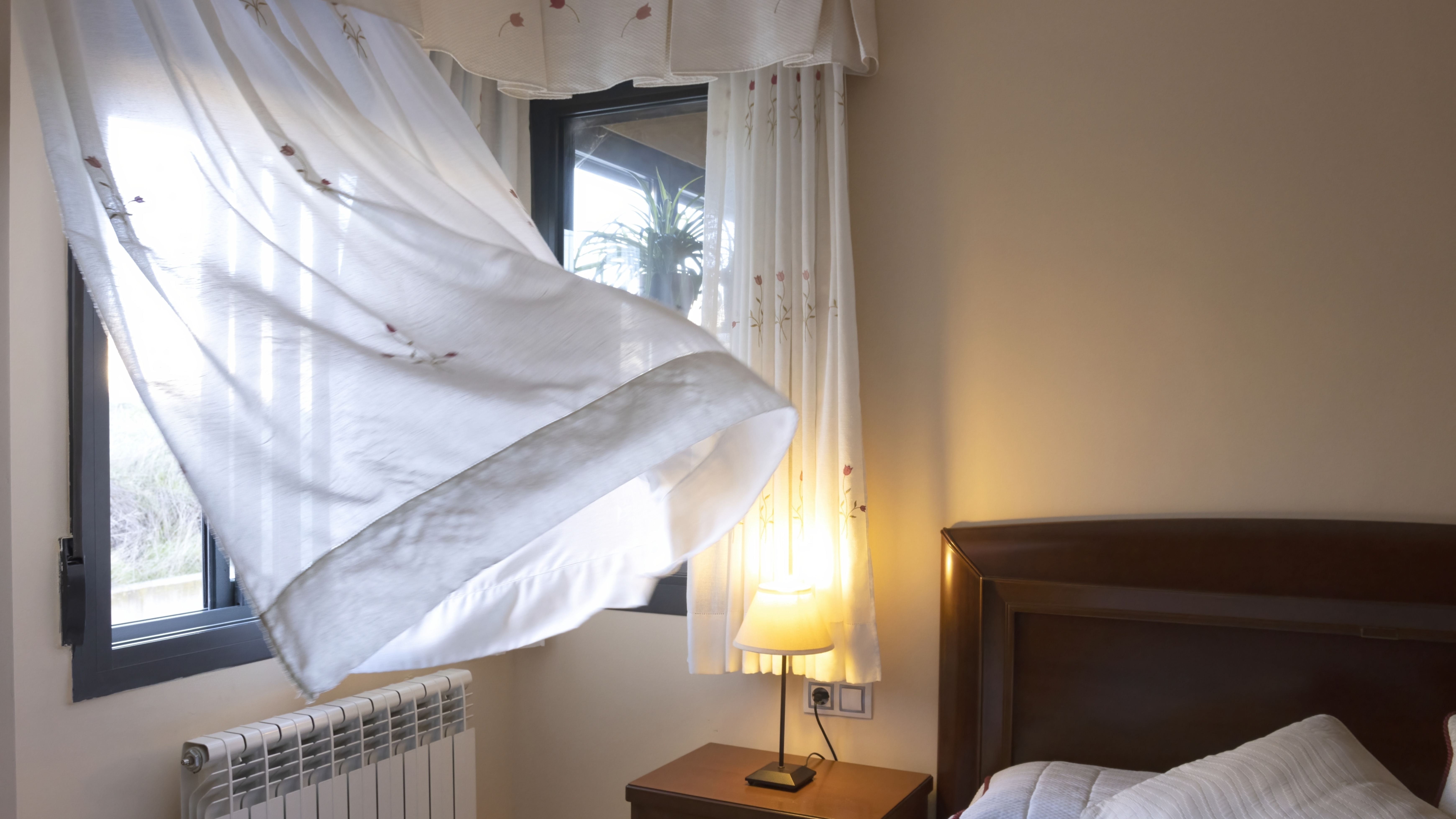 Wind blowing curtains through an open window in a bedroom