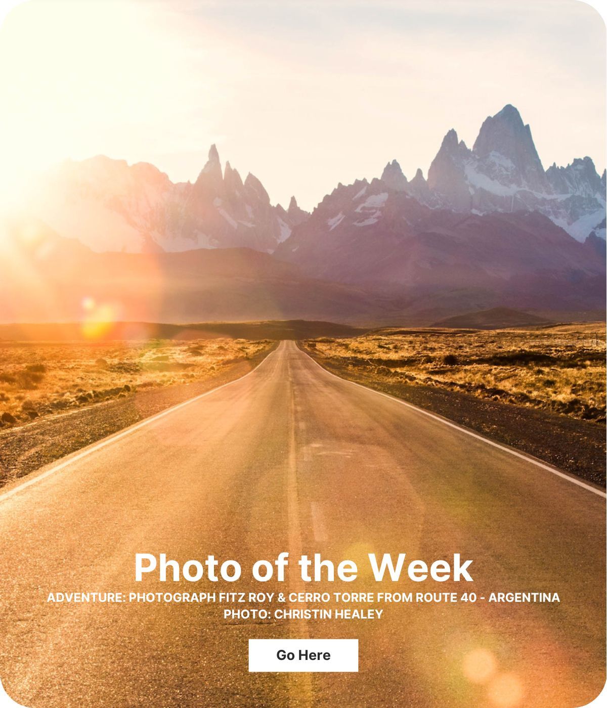 Looking down the middle of a road at jagged mountain peaks in the distance. The sun is creating a bright gold flare on the lens leading from the top left corner to the bottom right.