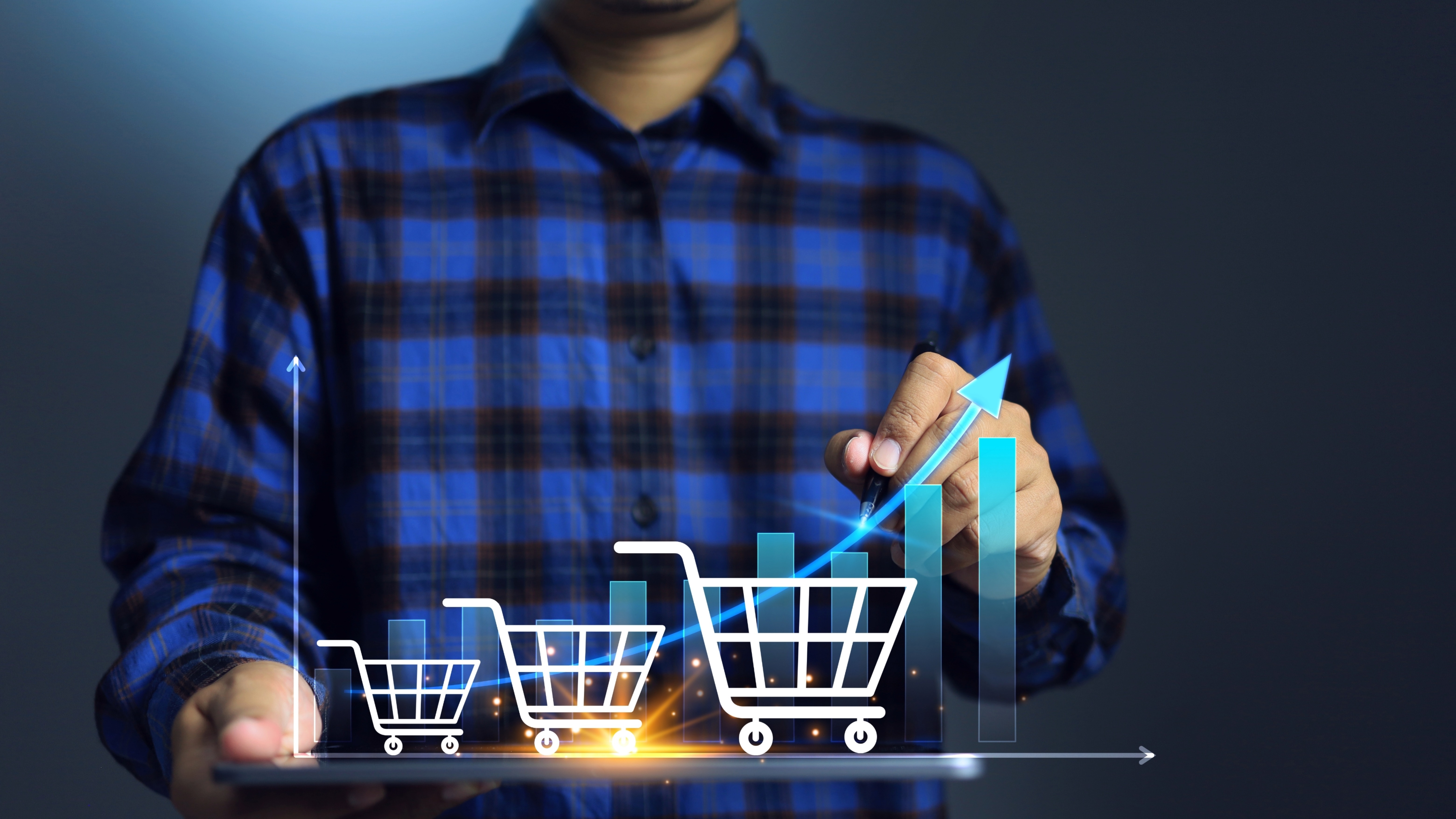 Man wearing a blue flannel shirt with three white shopping carts in graduating sizes with a bar chart behind them.