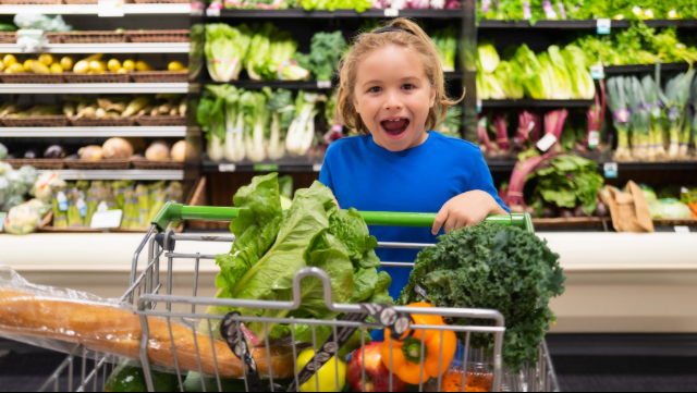 Girl pushing a grocery cart that is full and she has an open mouth surprised look. 