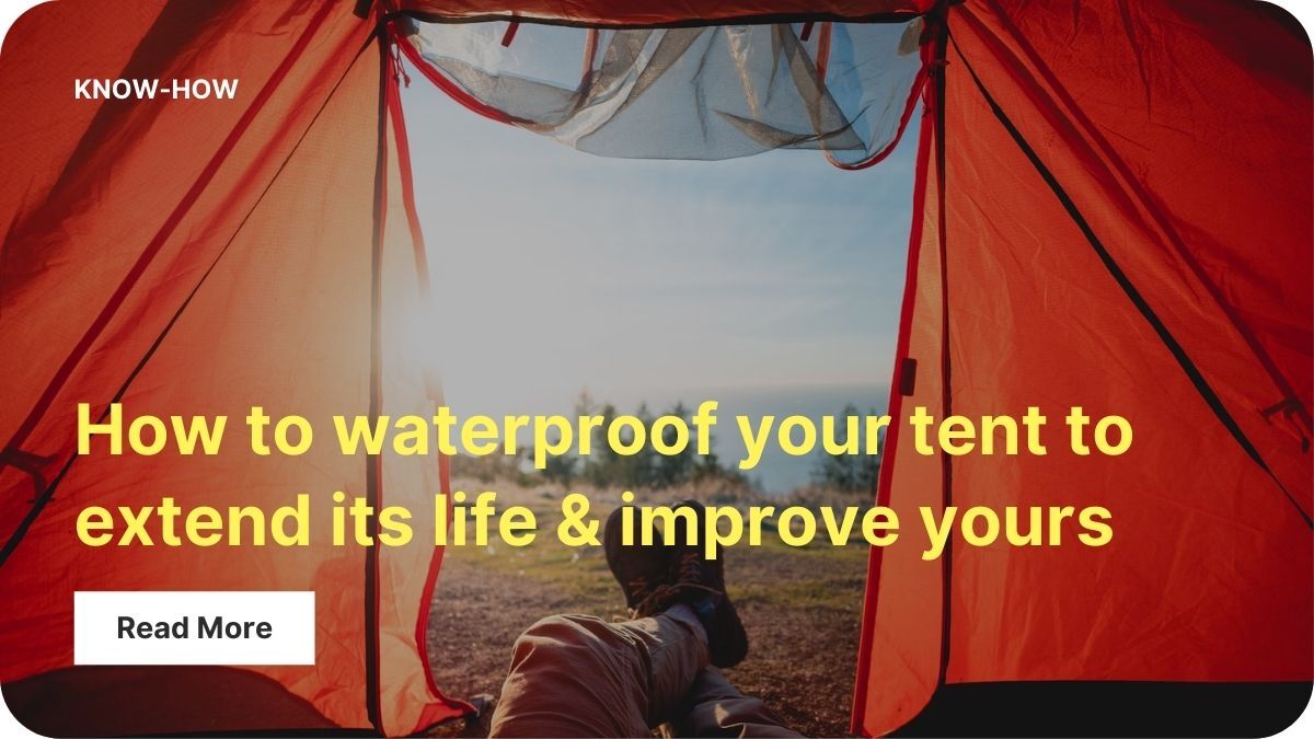 The photographer is lying half inside a tent with their legs through the door. Their feet are crossed and there are evergreen trees in the distance. The interior of the tent is bright orange.