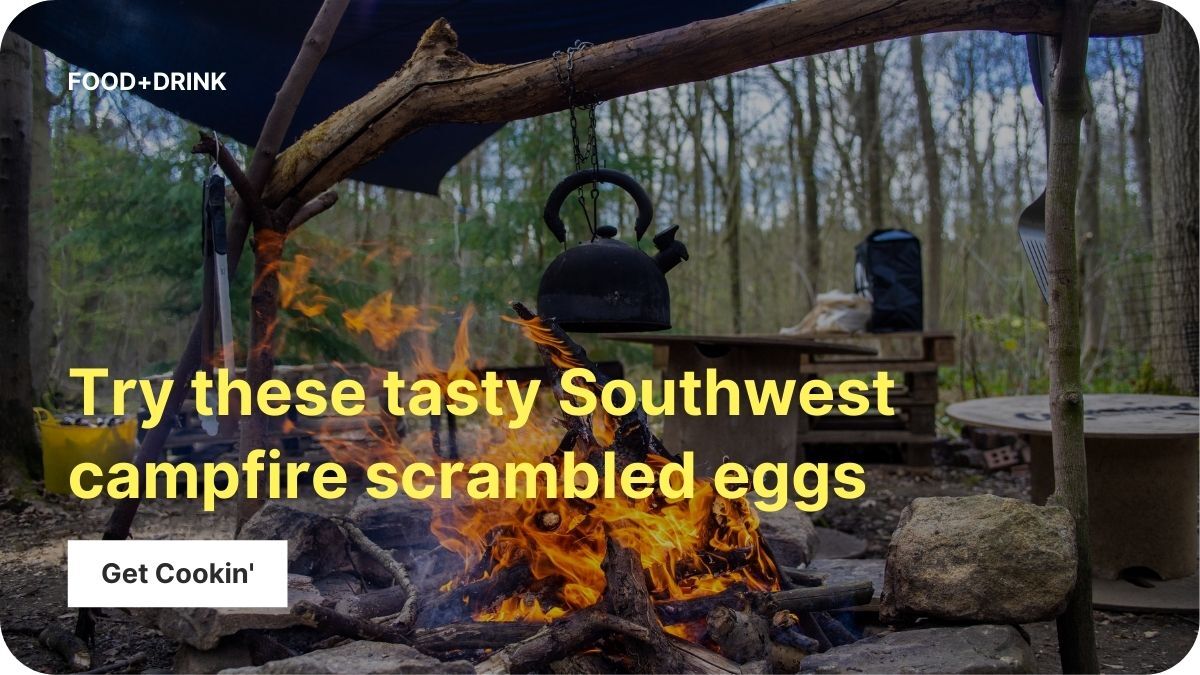 A campfire burns with a tea kettle perched on a table nearby. There are trees in the background.