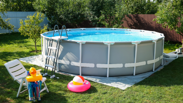 Above ground pool set up in a yard with toys around it. 