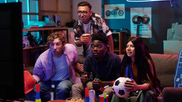 Four young people sitting on a couch, watching a soccer game. 