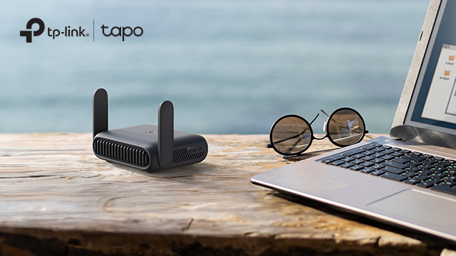 TP Link router on a bench overlooking the ocean with a laptop and sunglasses sitting beside it. 
