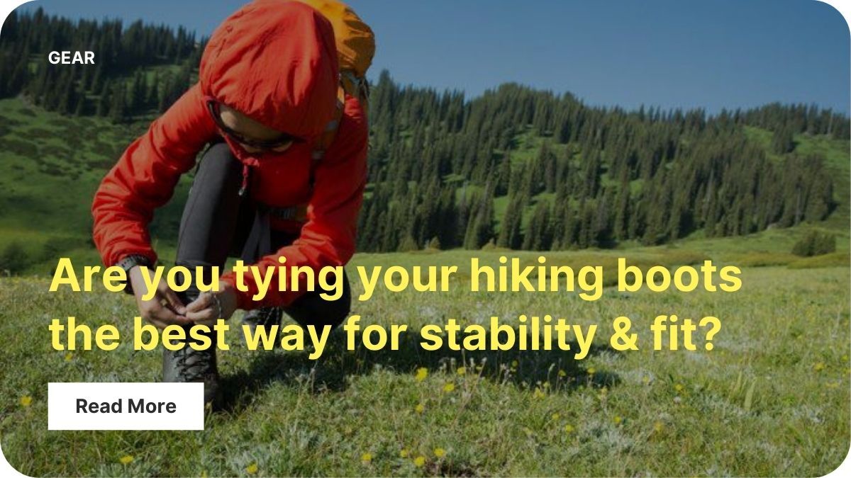 A person is backpacking out near mountains with evergreen trees. They're kneeling in a field at the base of the incline to tie their shoe.