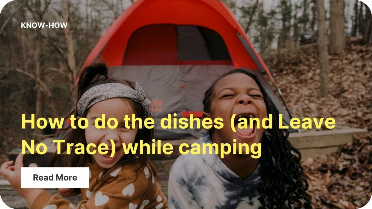 Two young kids are laughing with their mouths wide open in joy in front of a grey and red tent in the woods.