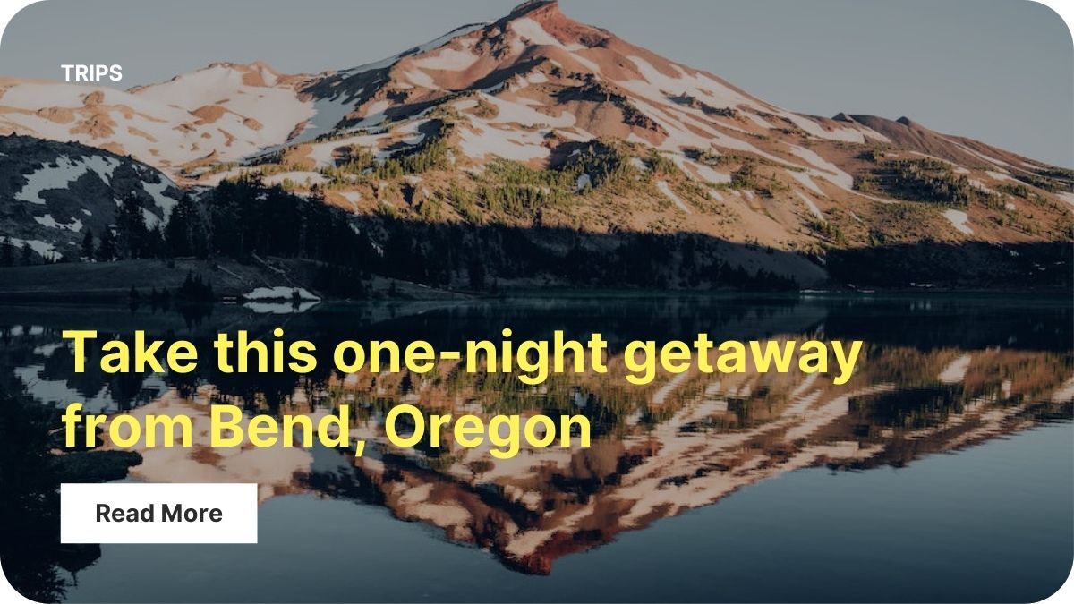 Three tall mountain peaks are dotted with snow. A lake meets the base of the mountains and reflects the peaks on it's glassy surface.