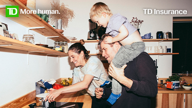 Man with toddler on his shoulders and a woman putting a pot on the stove.  There are wood shelves and wooden cabinets. 