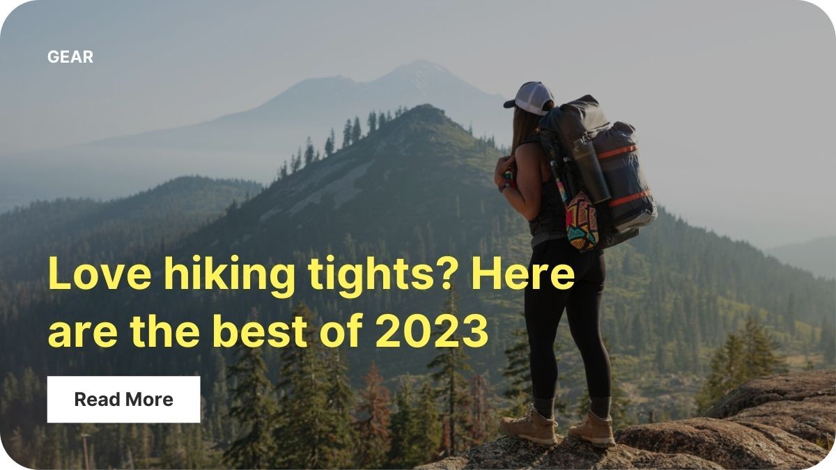 A person with a hiking backpack is standing on the edge of a rock cliff lookout out at mountains in the distance.